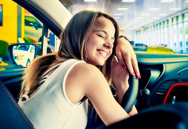 a young woman hugging the steering wheel of her first car smiling happily